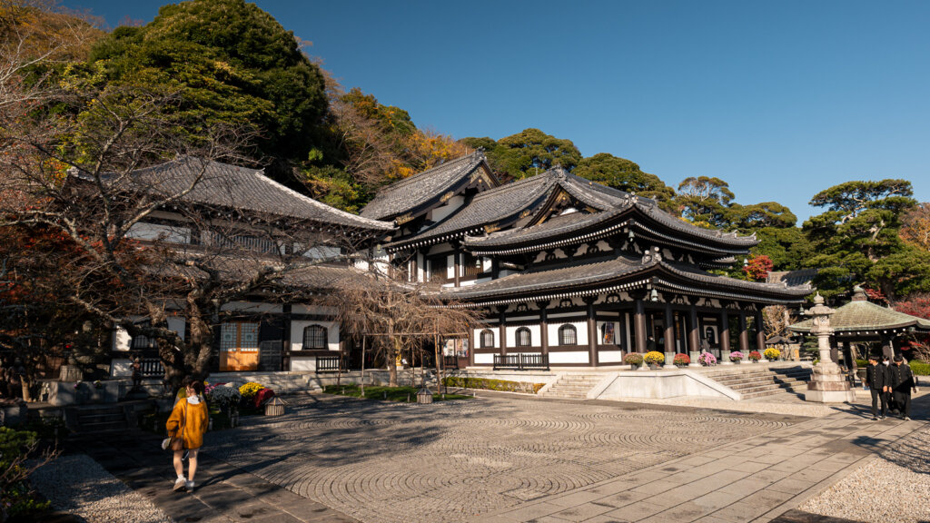 Courtyard at Hase-dera Temple in Kamakura with stone lanterns, seasonal foliage, and visitors moving between temple halls.