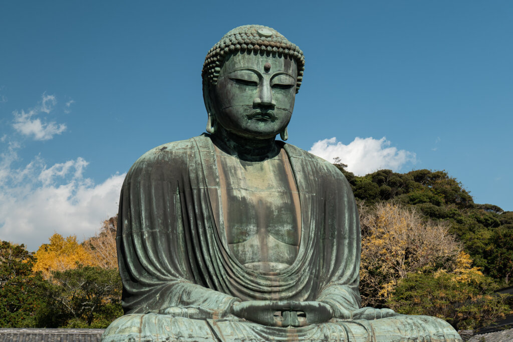 The Great Buddha (Daibutsu) at Kotoku-in Temple in Kamakura, surrounded by autumn foliage under a clear sky.