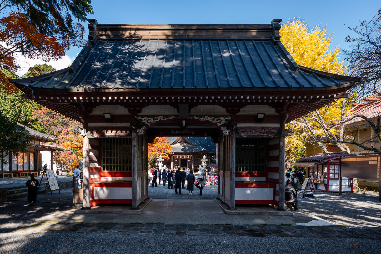 Gate with autumn foliage and visitors at Fuji Omuro Sengen Shrine