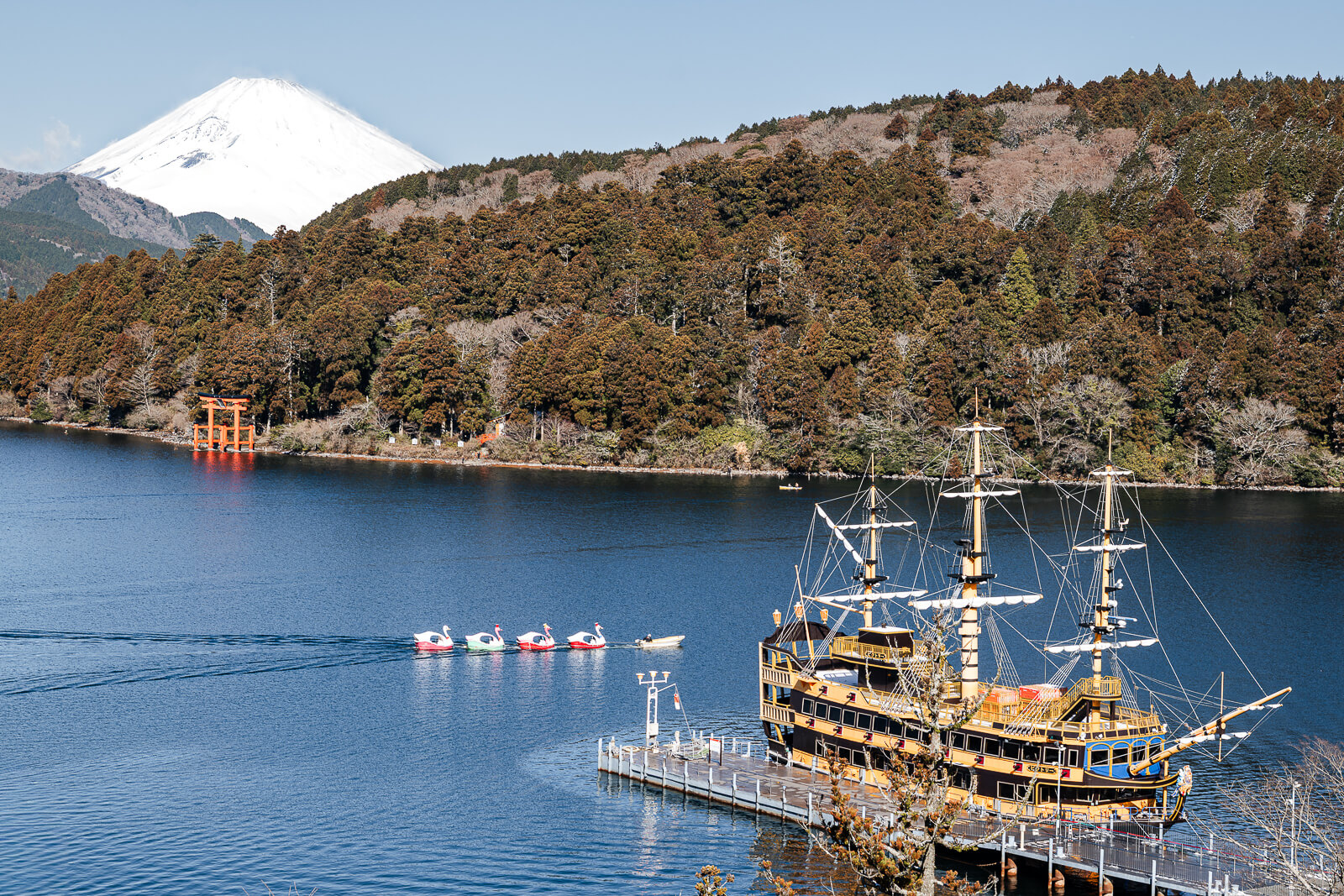 Lake Ashi in Hakone with the sightseeing pirate ship, Hakone Shrine torii gate, forested shoreline, and Mount Fuji in the background.