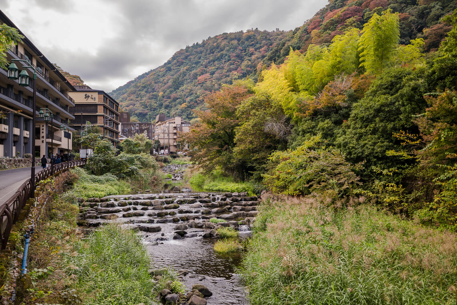 Sukumo River flowing through Hakone-Yumoto below wooded hills and buildings with developing autumn foliage.