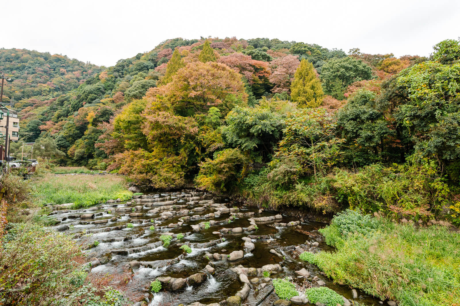 Rocky Sukumo River in Hakone-Yumoto framed by wooded hills showing mixed green and autumn foliage.