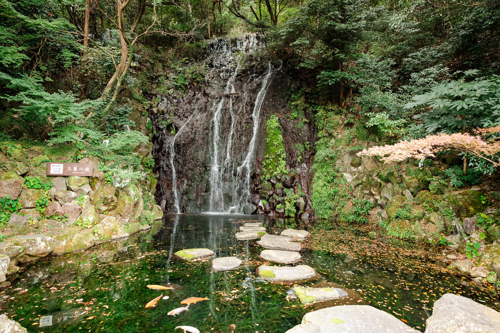 Hien Falls flowing over a dark rock face beside stepping stones and dense greenery in Tenseien Garden.
