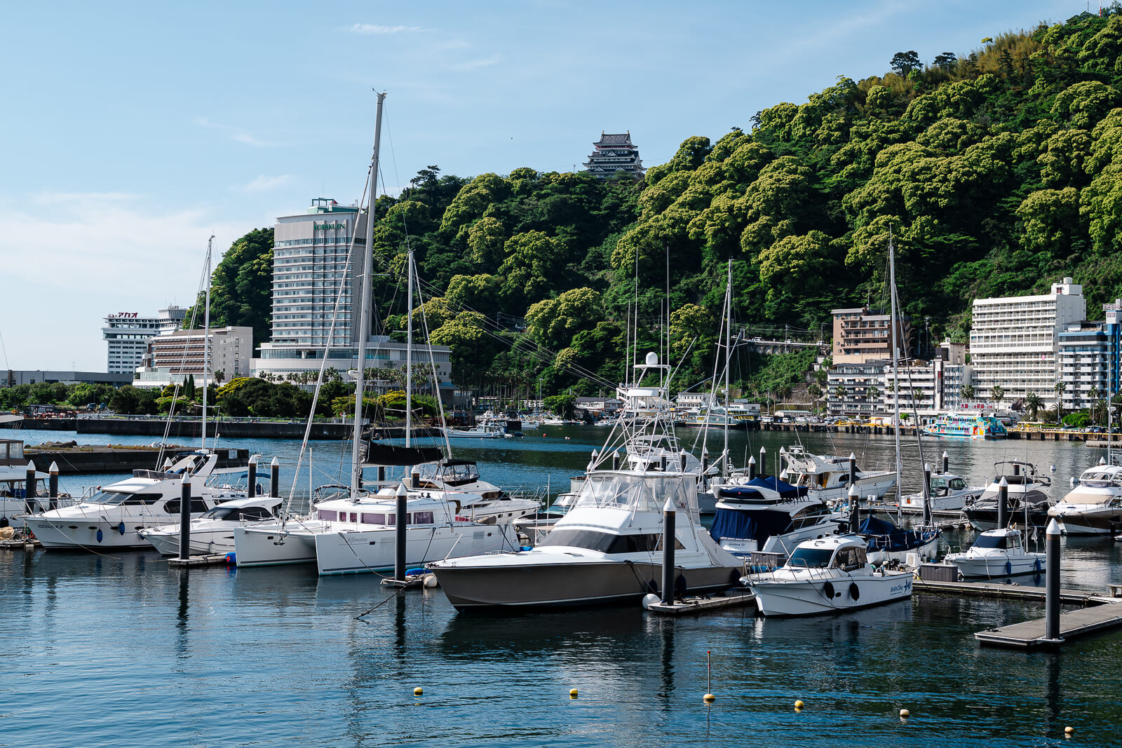 Atami Castle above Atami harbor with boats, hillside greenery, and waterfront hotels below.