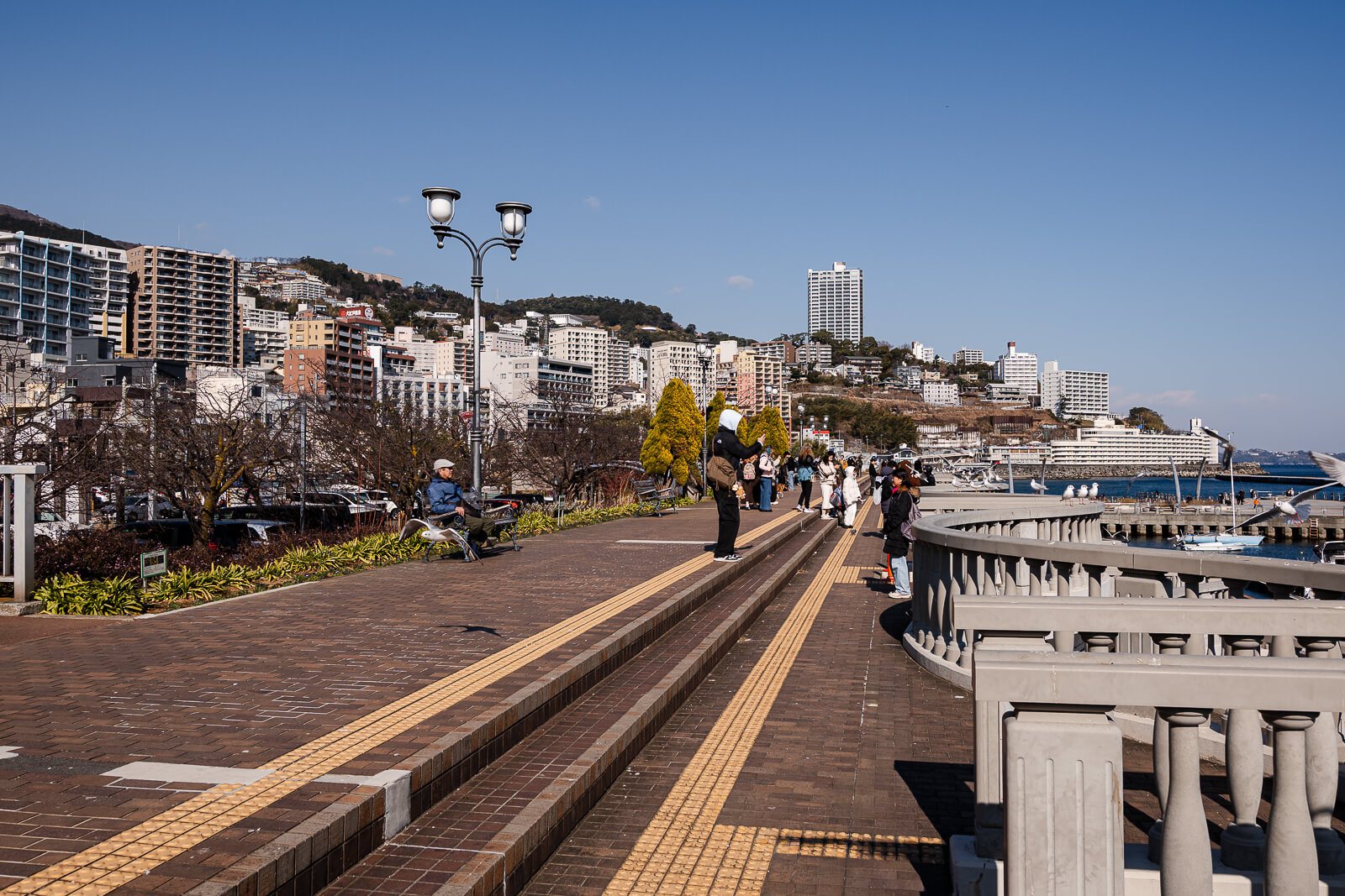 Waterfront promenade beside Moon Terrace in Atami with visitors walking along the harbor and seaside path.
