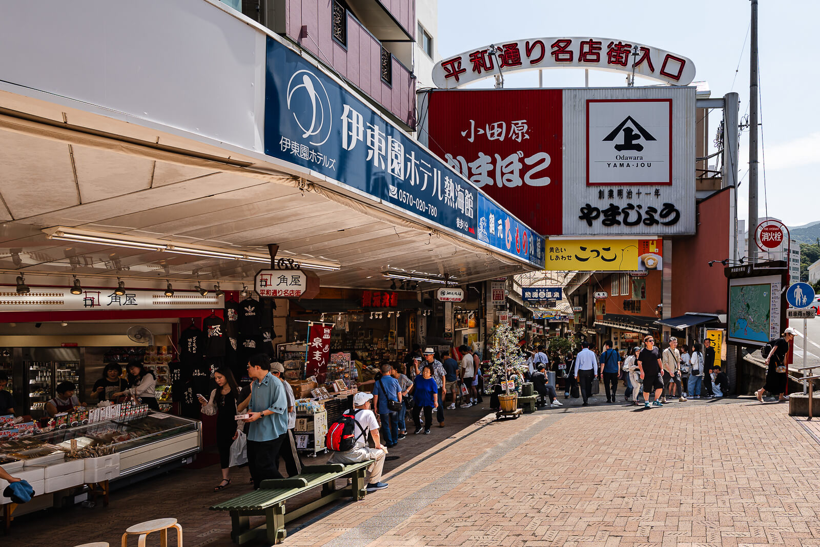 Entrance to Heiwa-dori shopping street near Atami Station, with food shops and visitors at the start of the downhill route.