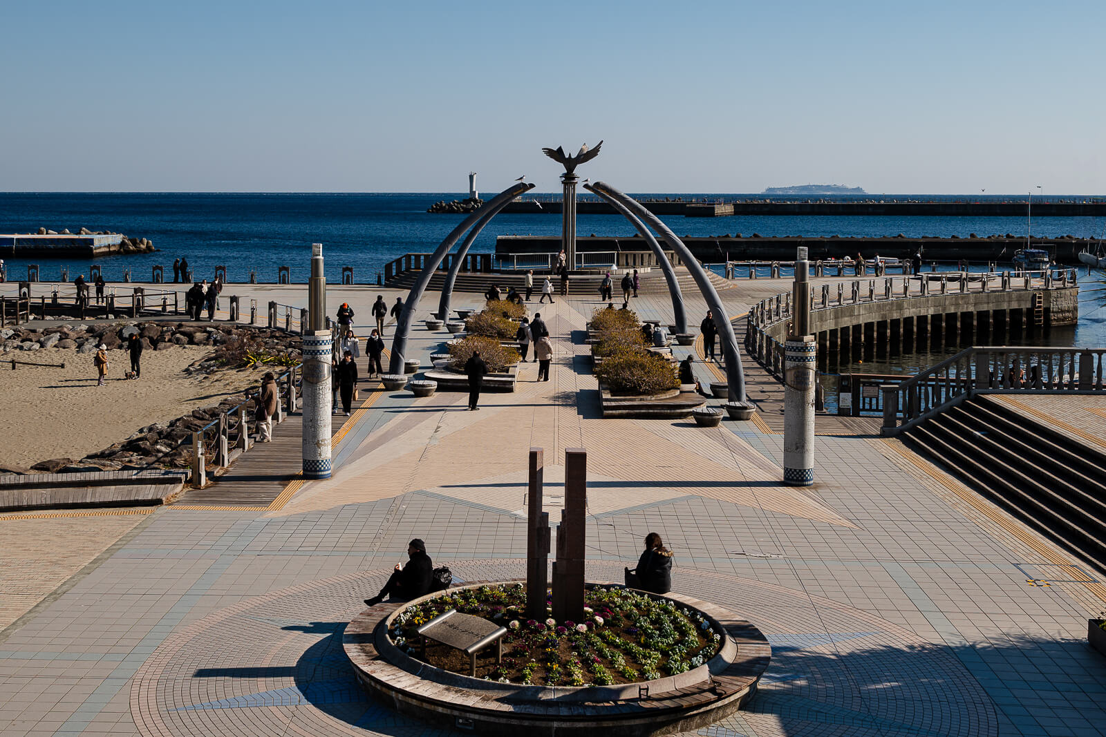 Moon Terrace waterfront plaza in Atami with visitors walking near the sea and harbor.