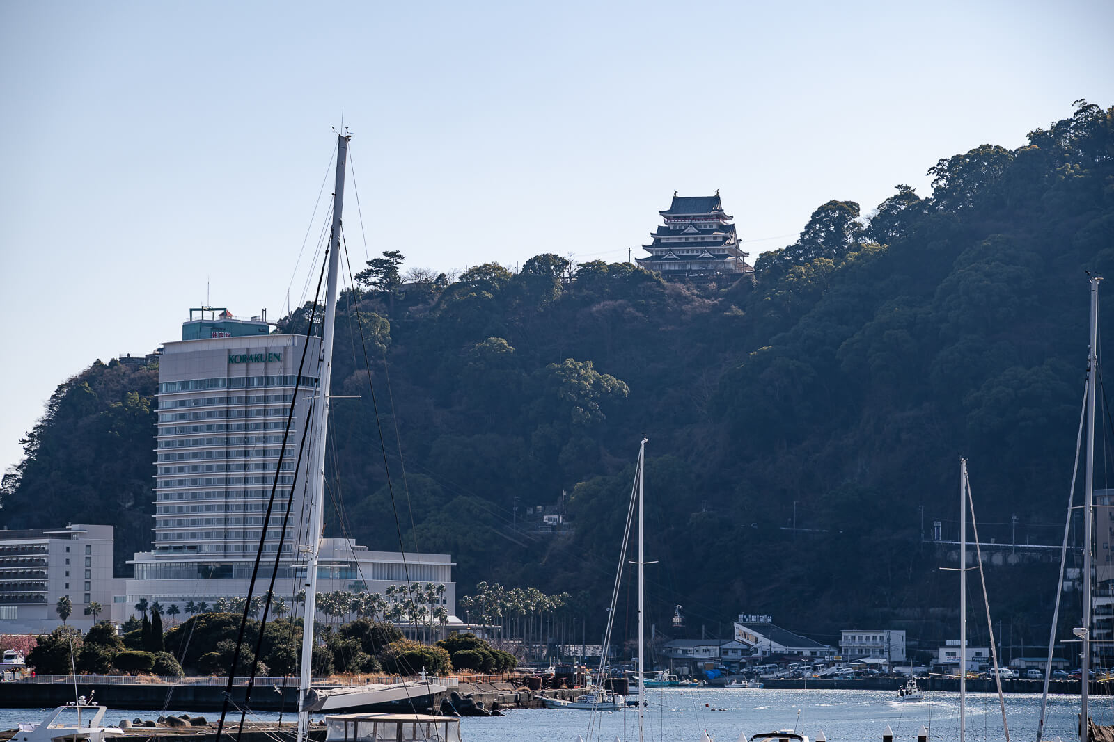 Atami harbor with hotel, hillside buildings, ropeway, and Atami Castle above the coastline
