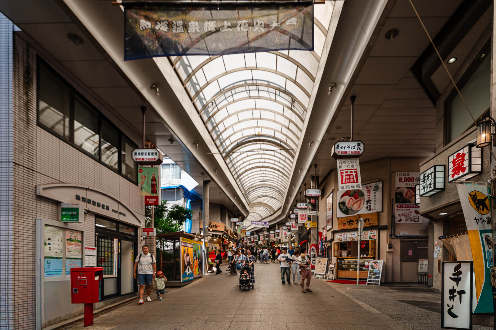 Covered shopping street near Atami Station with food shops, signs, and visitors walking through the arcade.