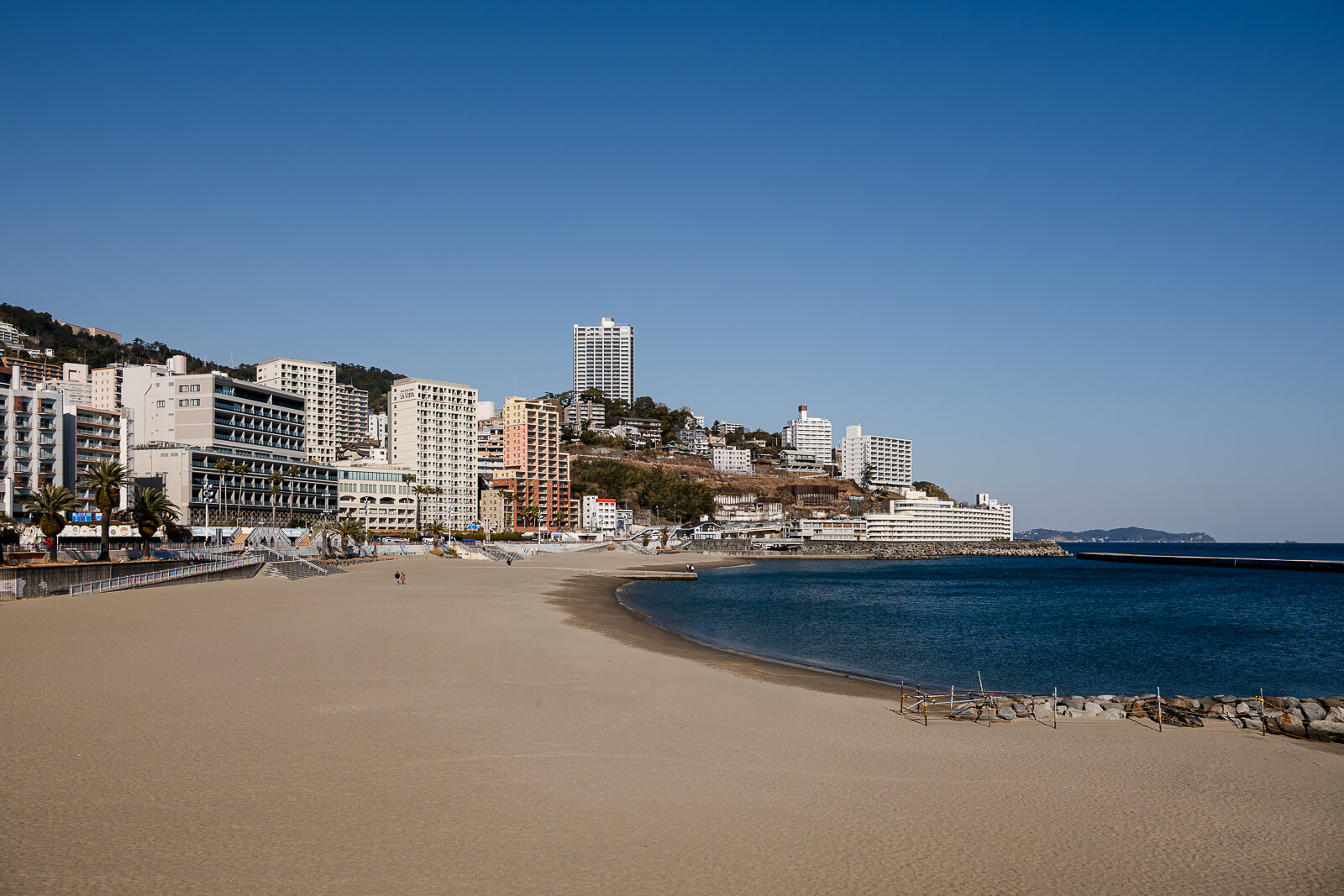 Wide view of Atami Sun Beach with the waterfront hotels and hillside cityscape behind it.