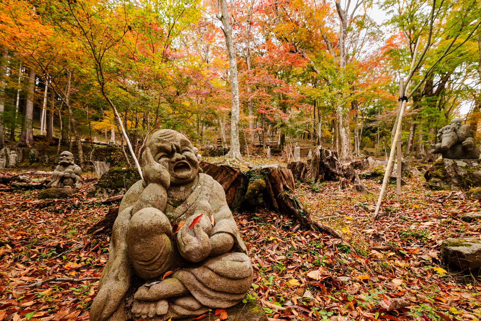 Expressive seated rakan statue among autumn leaves at Choanji Temple