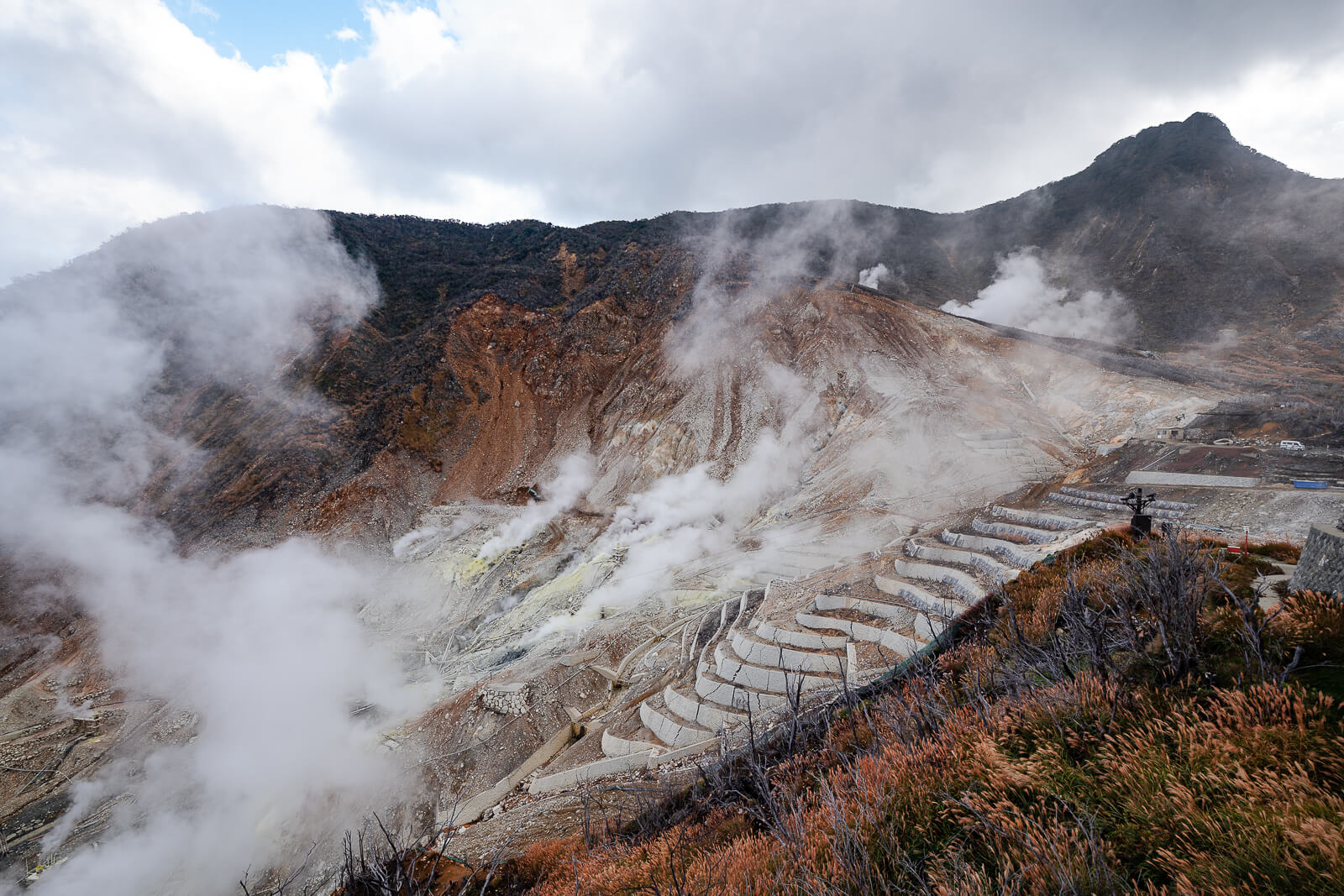 Steam drifting across Owakudani under cloudy skies with shifting visibility