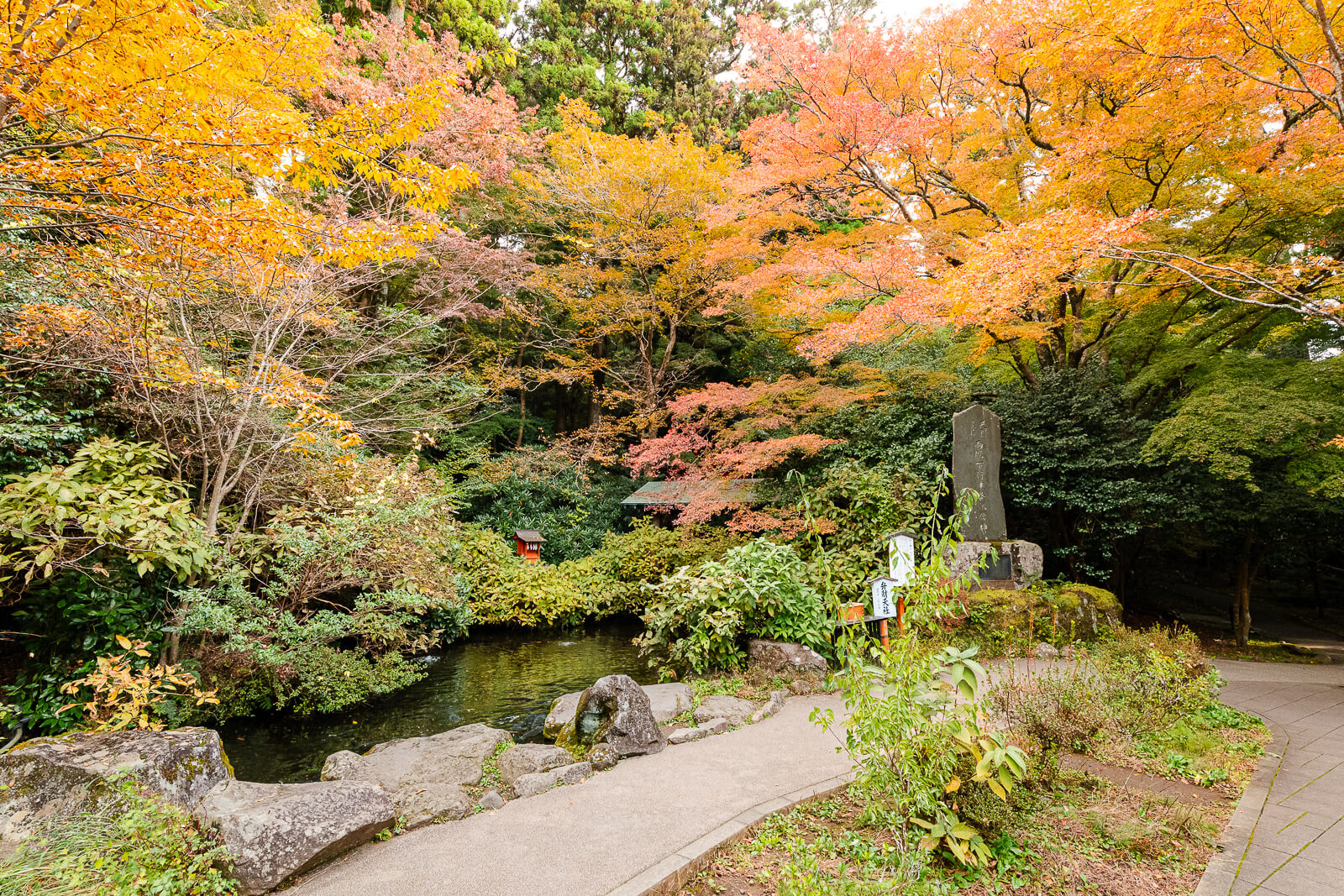Stone path and pond surrounded by yellow and orange autumn foliage at Hakone Shrine
