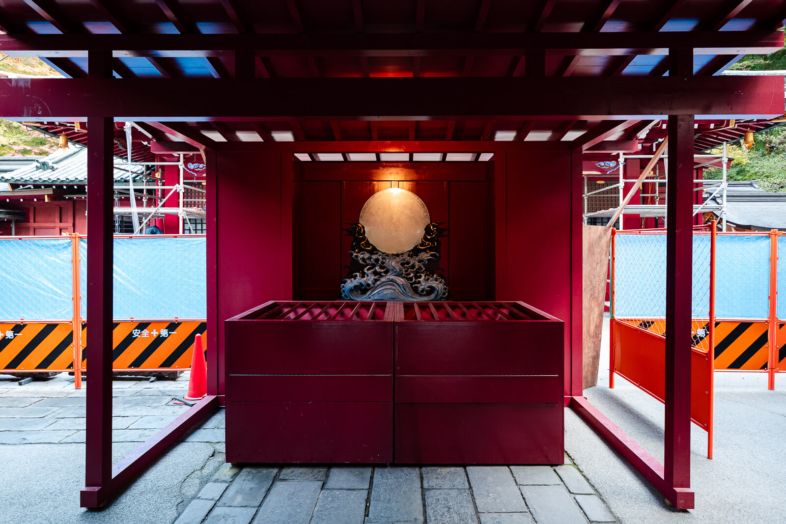 Round mirror above an offering area framed by red timber at Hakone Shrine in Motohakone
