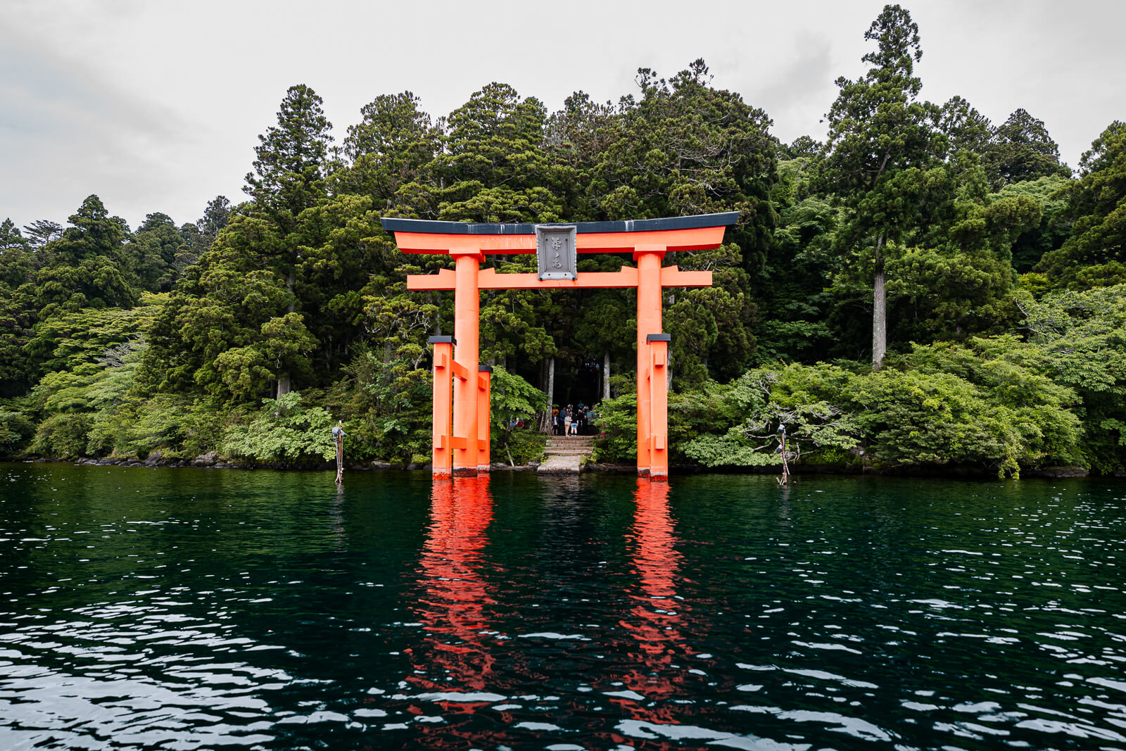 Heiwa no Torii in Lake Ashi, seen from a boat with the wooded shore of Hakone Shrine in Motohakone behind it
