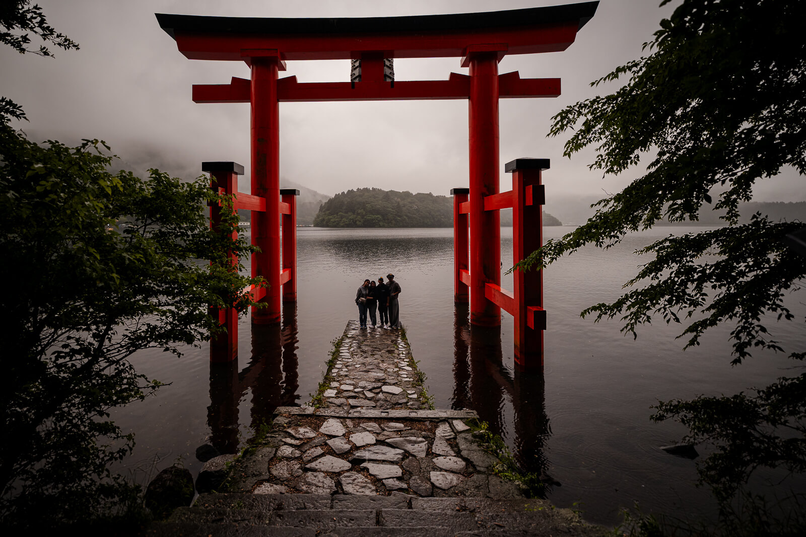 Heiwa no Torii framing Lake Ashi and visitors on its stone platform at Hakone Shrine in Motohakone