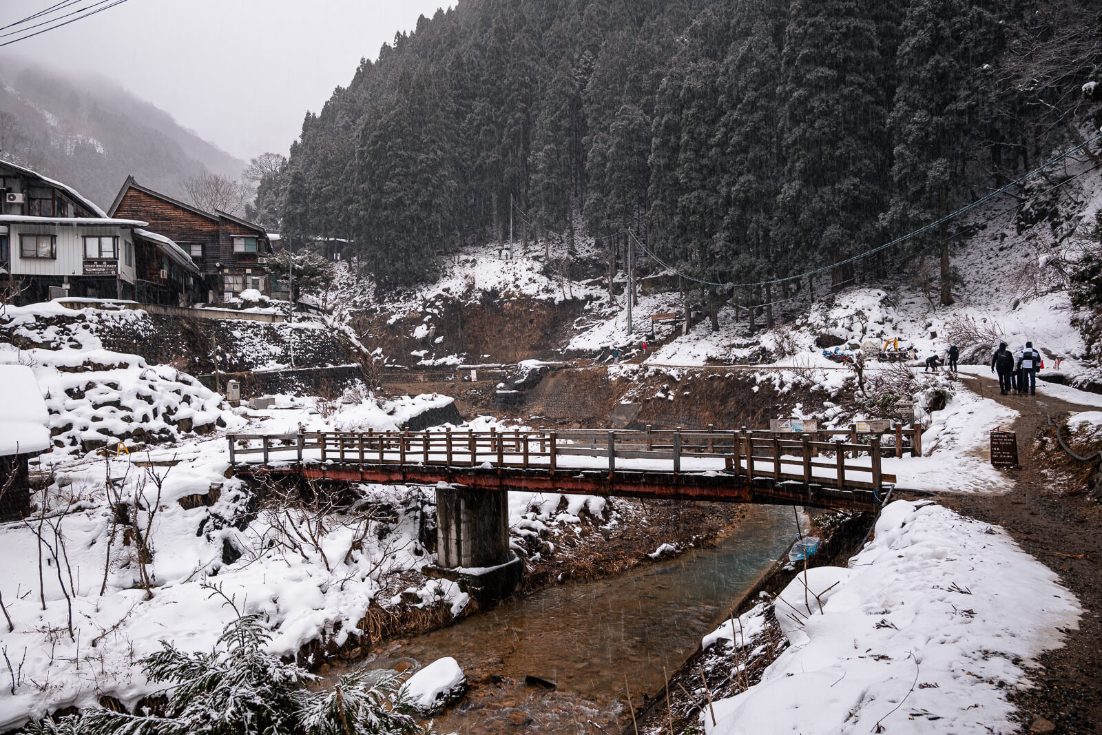 Red pedestrian bridge crossing a snowy river valley near Jigokudani Monkey Park