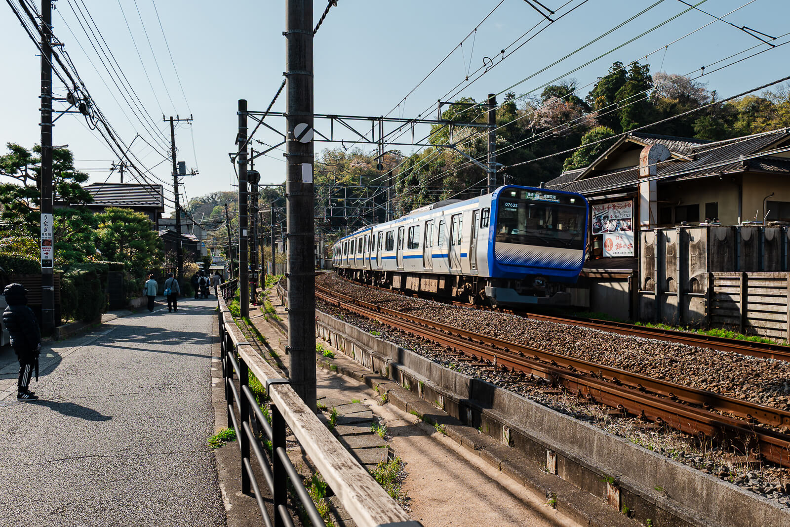 Pedestrians walking along a narrow street beside the JR railway near Engaku-ji Temple