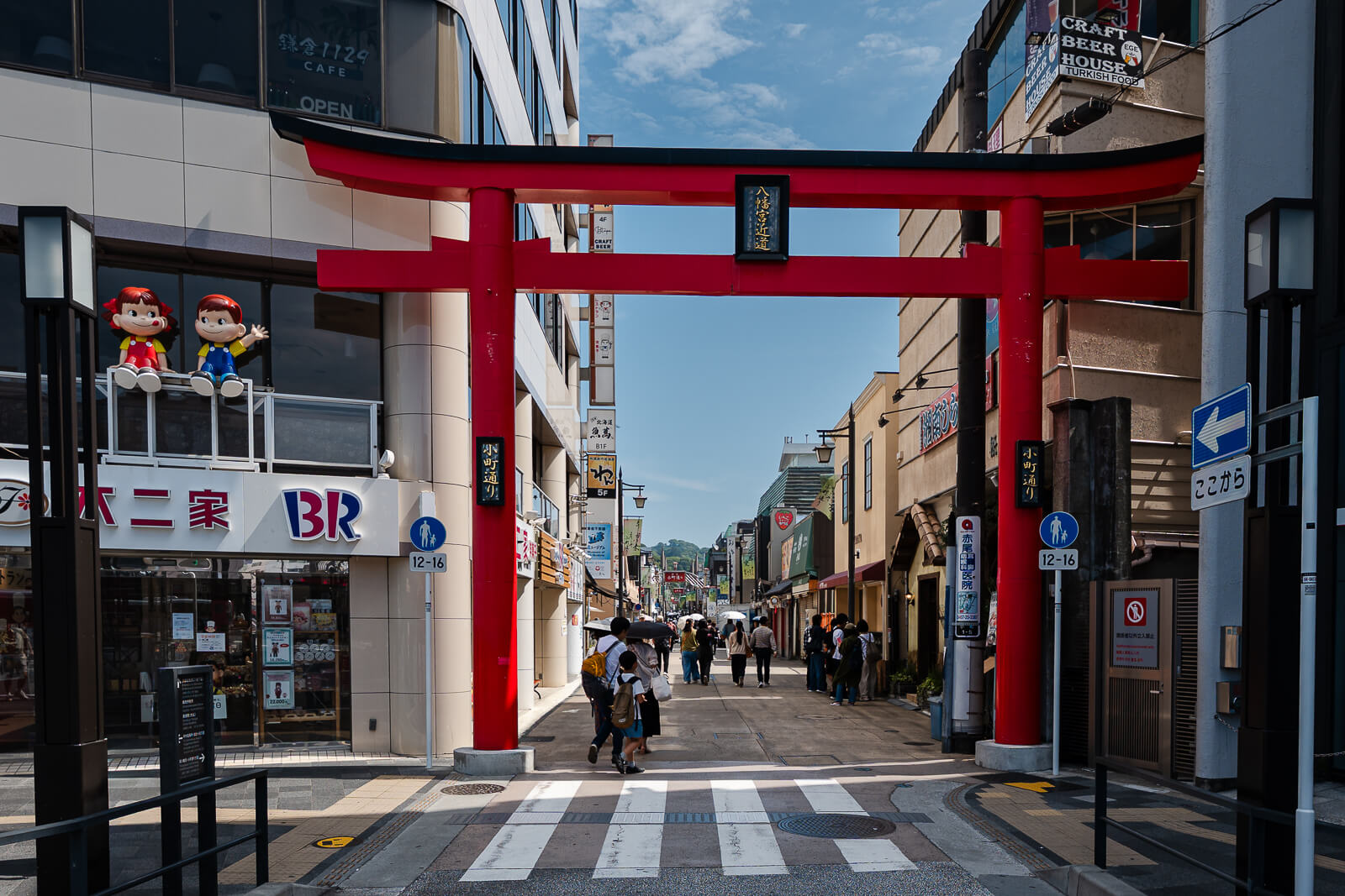 Red torii marking the entrance to Komachi-dori with pedestrians and shops in central Kamakura