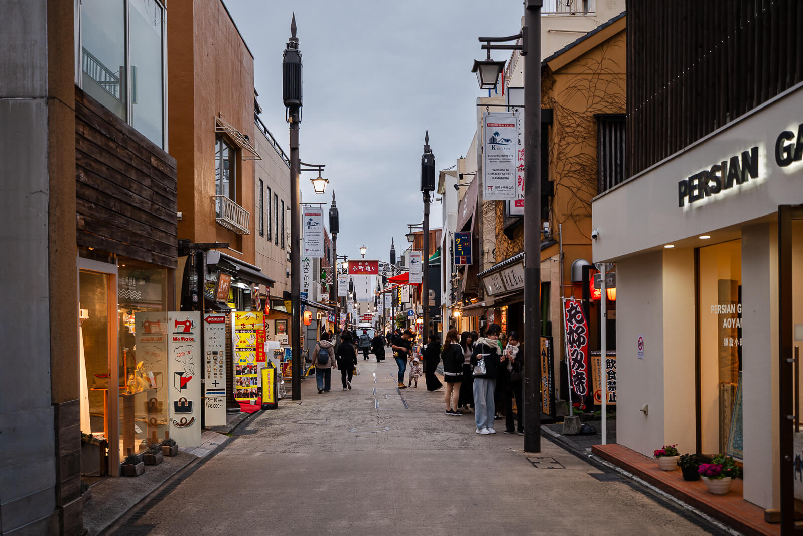 Komachi Street entrance sign above pedestrians and illuminated shops in central Kamakura during the evening