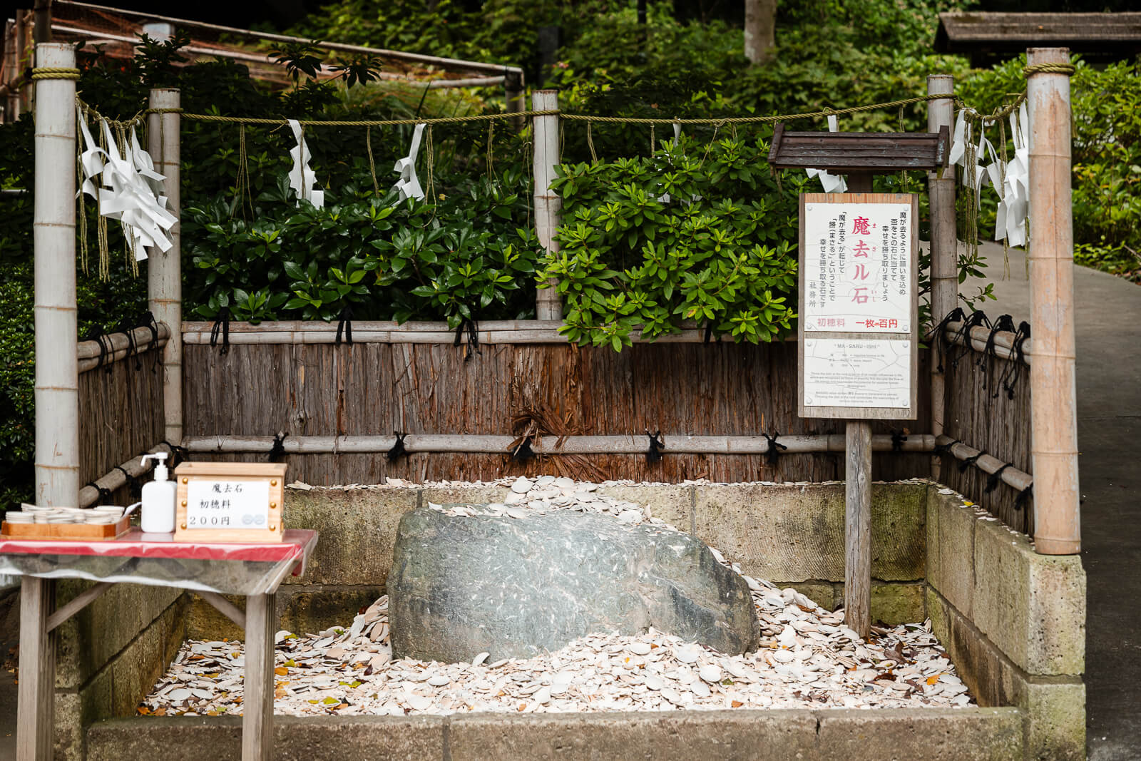 The Masaru Stone is surrounded by broken earthenware dishes near the entrance to Kuzuharaoka Shrine