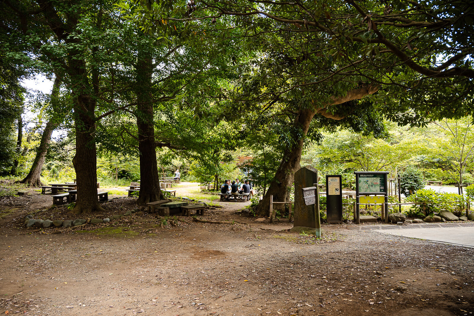 A shaded entrance leads into Kuzuharaoka Shrine from Genjiyama Park beneath dense summer trees