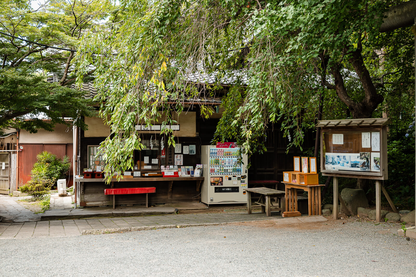 The shrine office, vending machine, and information boards stand beneath trees at Kuzuharaoka Shrine