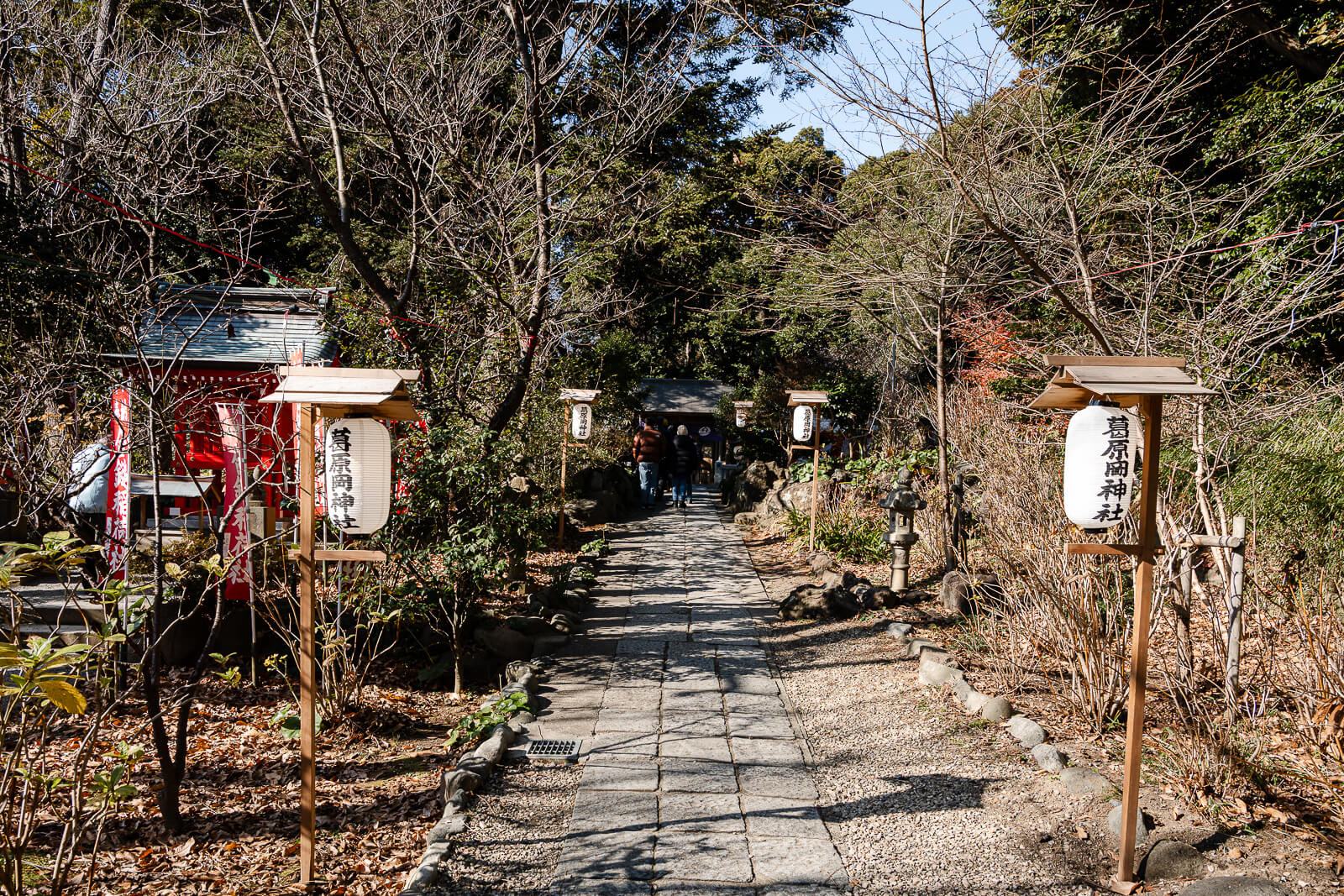 A stone path lined with lanterns leads toward the main shrine at Kuzuharaoka Shrine in winter