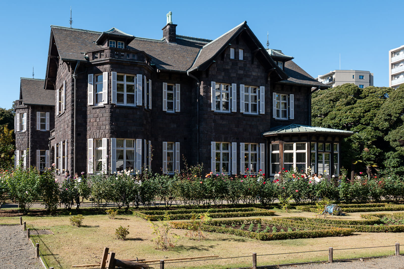 The Western-style mansion at Kyu-Furukawa Gardens stands against blue sky, with its dark stone exterior seen from the grounds.