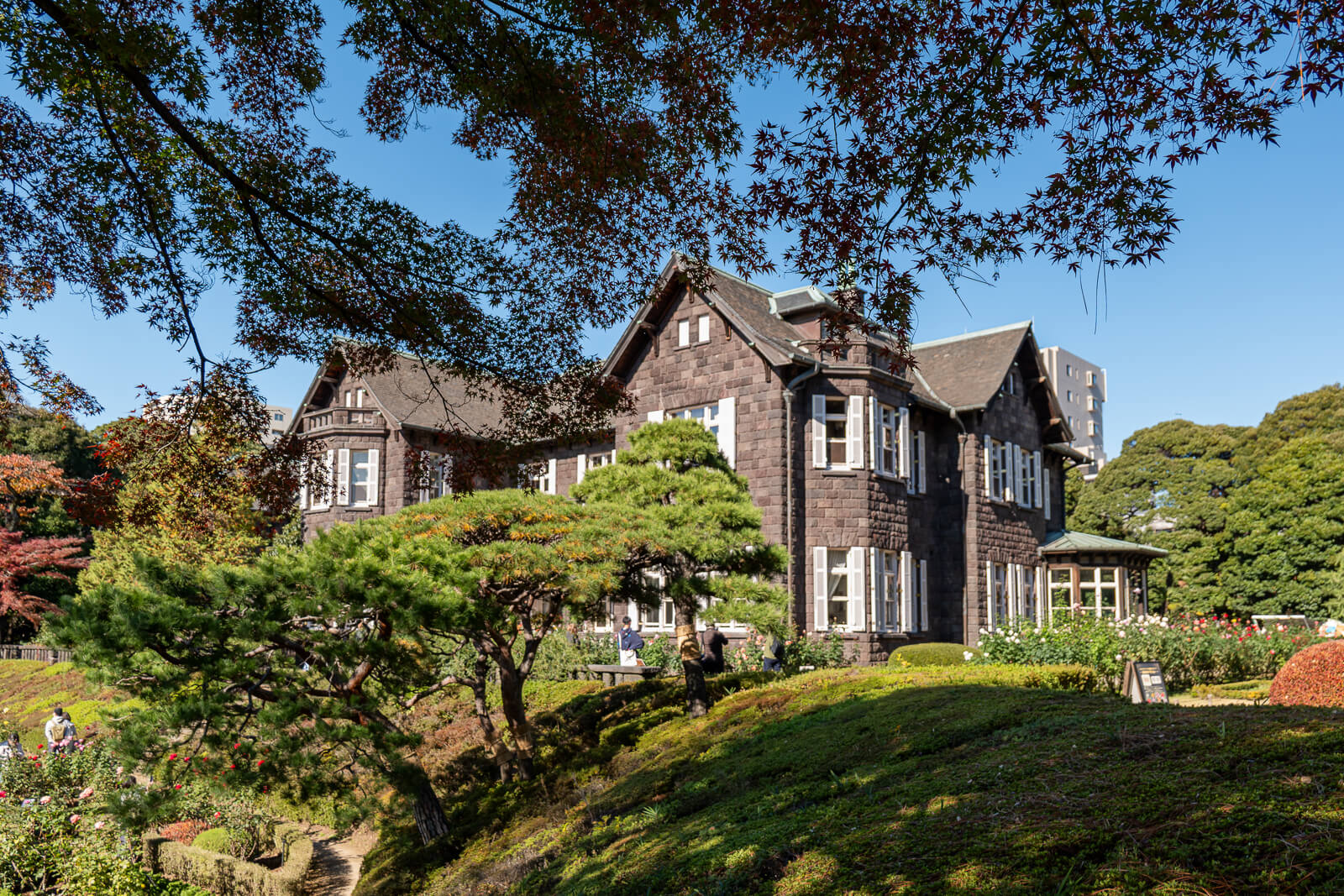 A side angle shows the Western-style mansion at Kyu-Furukawa Gardens behind trees, shrubs, and the upper garden lawn.