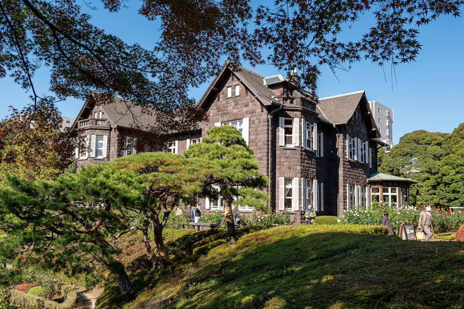 The stone mansion at Kyu-Furukawa Gardens appears between trees and garden plantings, with a clear autumn sky above.