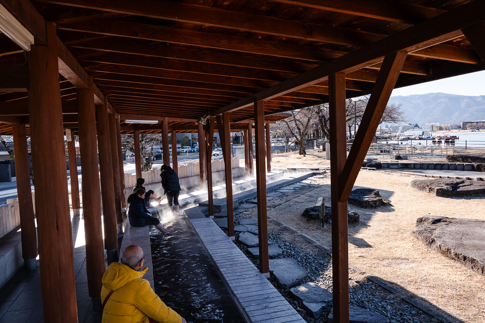 Visitors sitting inside the footbath pavilion beside Lake Suwa