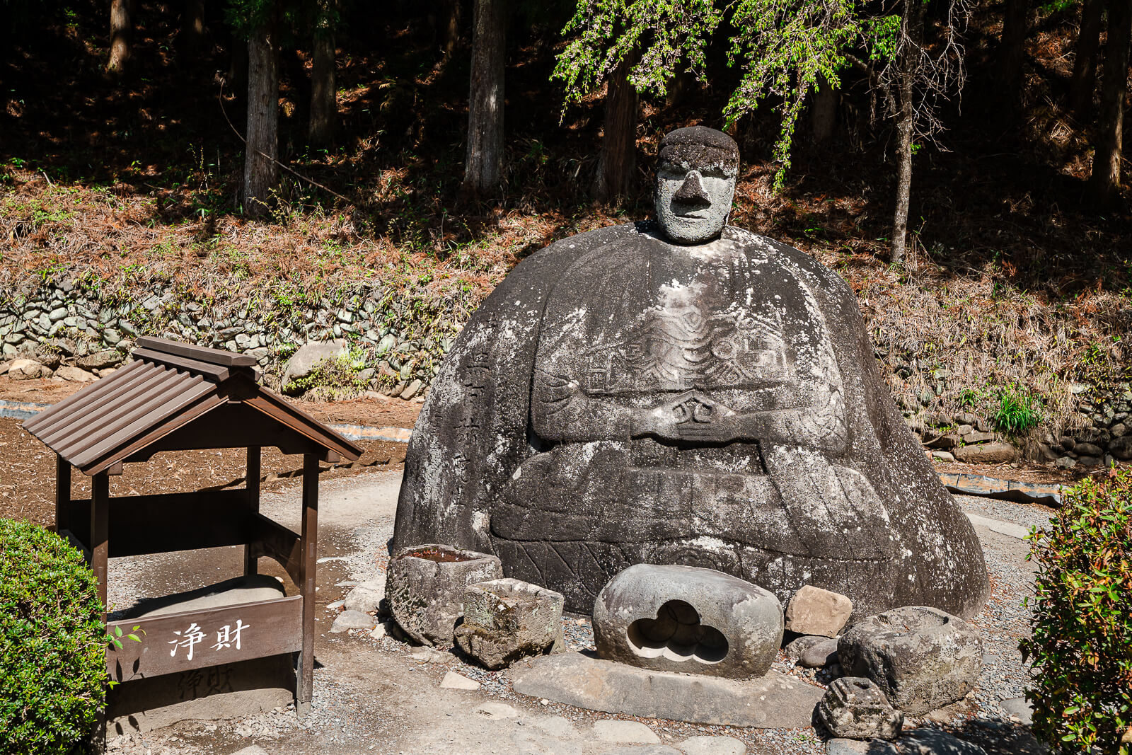 Manji Stone Buddha beside its small sign in Shimosuwa, Nagano Prefecture.