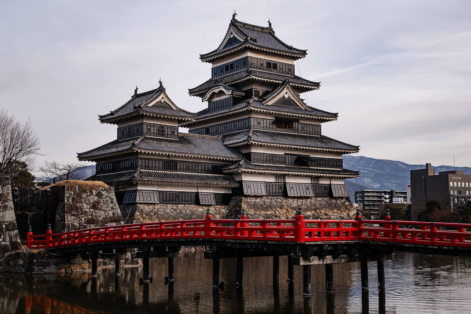 Matsumoto Castle with its black-and-white keep, red bridge, moat, and mountain backdrop in Nagano.